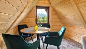 Interior de madera con una mesa redonda y cuatro sillas, una ventana con vistas a la montaña y una puerta con diseño decorativo.