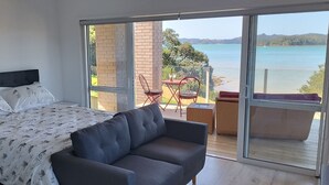 Ein Schlafzimmer mit einem Bett, einem grauen Sofa und einem Balkon mit Meerblick.