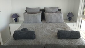 Ein ordentlich eingerichtetes Schlafzimmer mit einem Bett, zwei Nachttischen, zwei Lampen und Blick ins Freie.