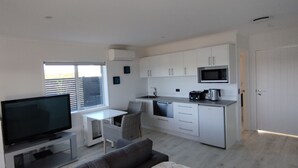 Eine moderne Wohnung mit Flachbildfernseher, Essbereich, Küche mit weißen Schränken und einem großen Fenster.