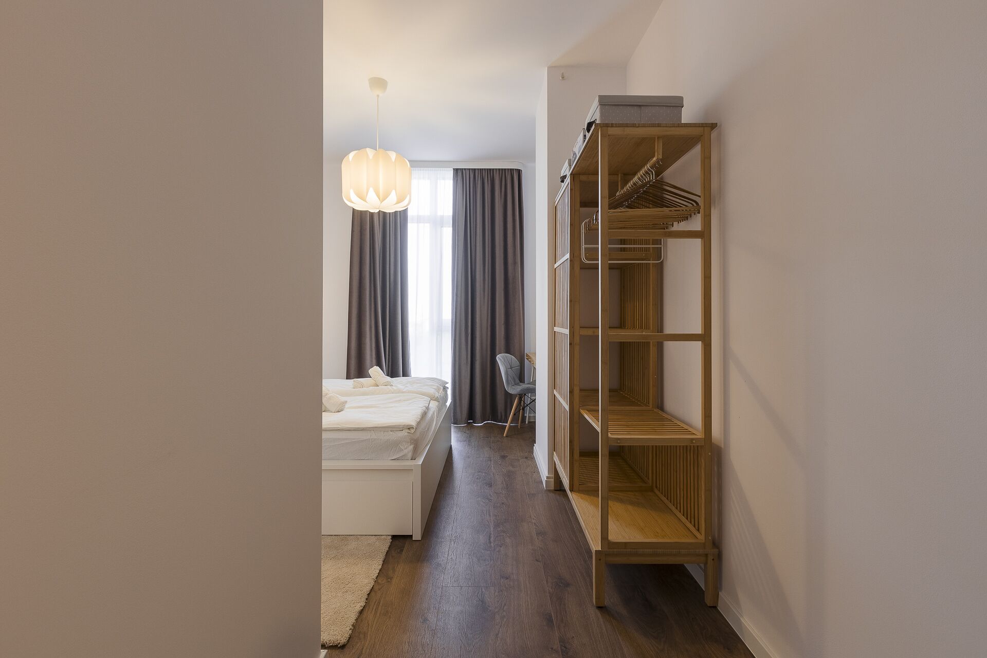 Une chambre d’hôtel avec un lit, une armoire en bois, un bureau et un luminaire suspendu.
