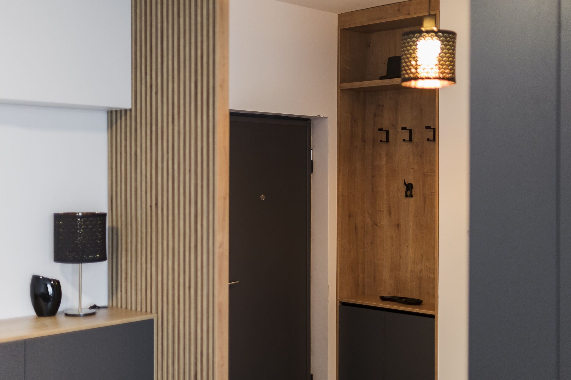 A modern interior with a wooden cabinet, a black door, and a pendant light.