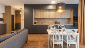 A modern kitchen with dark cabinetry, a wooden countertop, and a dining area with white chairs and a table. - Zoe Apartment (Timisoara)