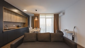 A modern kitchen with dark cabinets, a wooden countertop, and a built-in oven. There is a dining area with a table and chairs, and a sofa in the foreground. - Zoe Apartment (Timisoara)