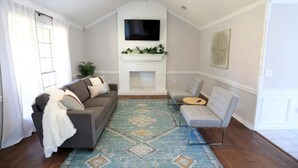 Una sala de estar con chimenea, un sofá, un sillón y un televisor montado en la pared.