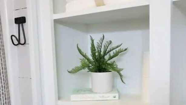 Un estante blanco con toallas dobladas y una planta en maceta.
