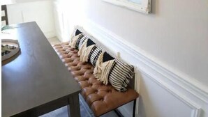 Un comedor con un banco, una mesa y un ventanal con marco blanco.