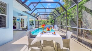 Un espace de restauration extérieur moderne, doté d’une véranda en verre, d’une piscine et d’une végétation luxuriante.