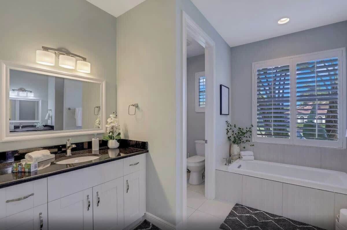 A bathroom with a double sink vanity, a large mirror, and a bathtub.