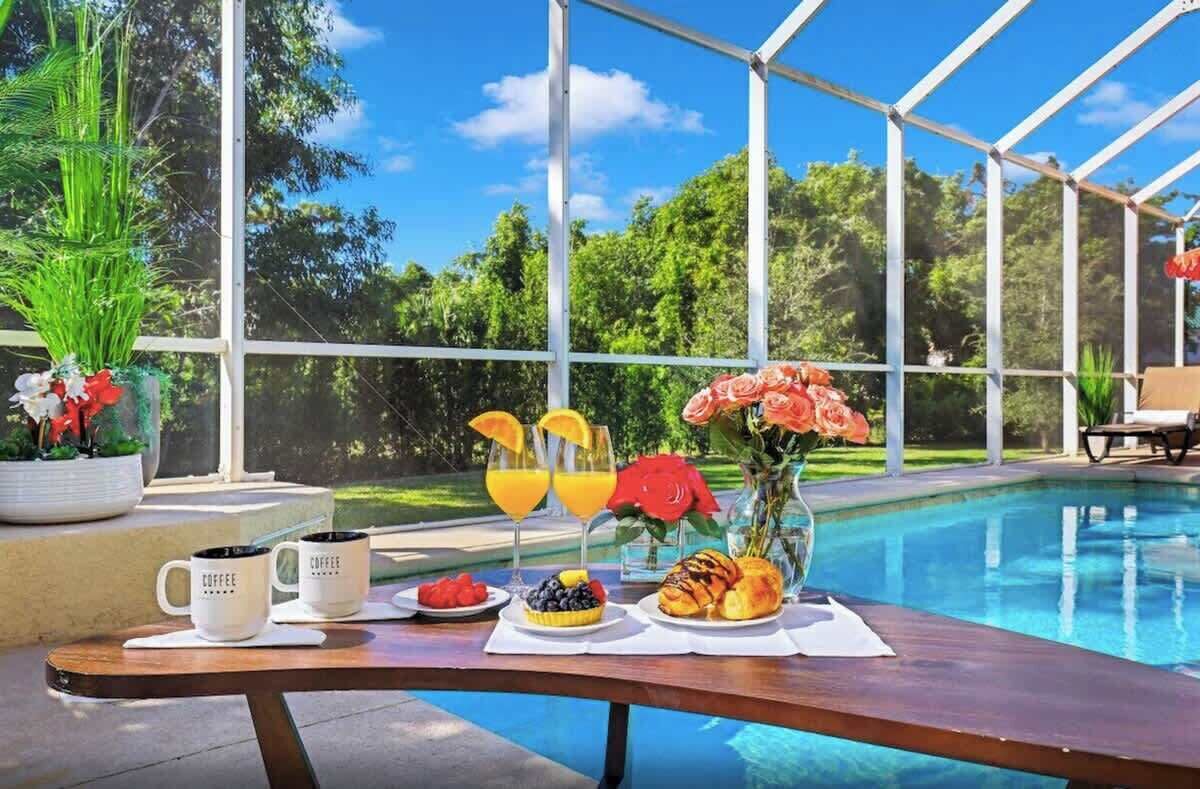 Ein Frühstückstisch an einem Pool mit Tassen, Früchten und Blumen.