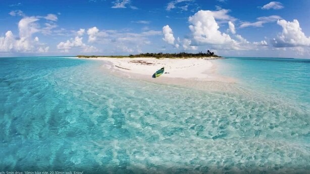 Una playa con agua turquesa cristalina, una orilla de arena y una pequeña isla a lo lejos.