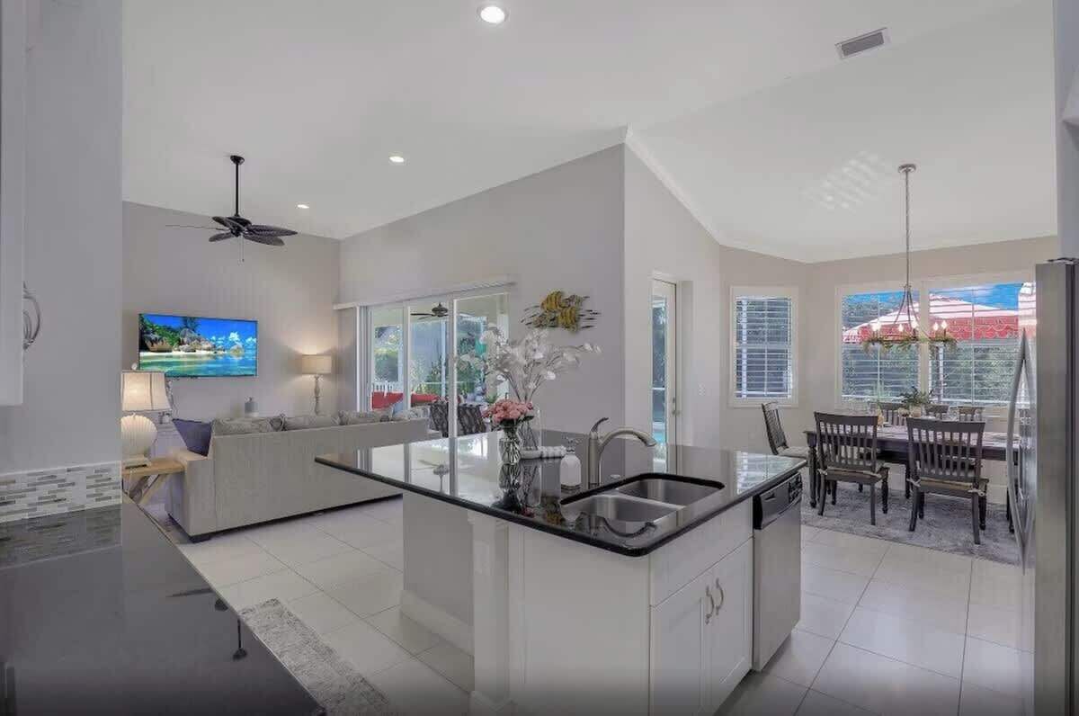 A modern kitchen with a central island, a dining area with a table and chairs, and a large window providing a view of the outdoors.