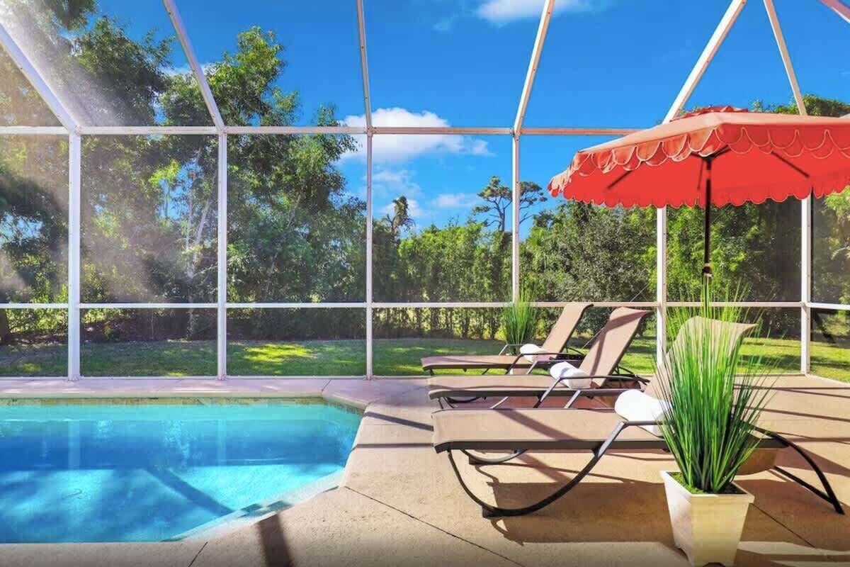A pool area with a glass enclosure, lounge chairs, and a red umbrella.