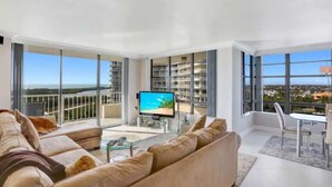 A modern living room with a large sofa, a flat-screen TV, and a dining area with a table and chairs.