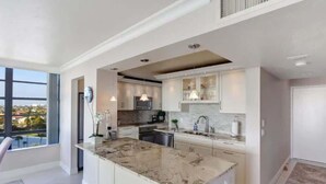 A modern kitchen with white cabinetry, a marble island, and pendant lighting.
