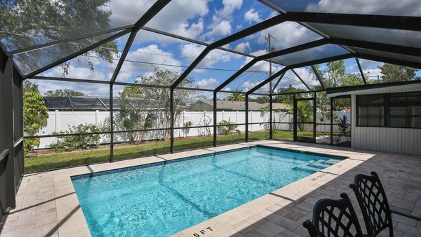 A covered swimming pool with a 5ft depth marker, surrounded by a patio area with chairs.