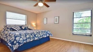 A bedroom with a bed, a ceiling fan, and two windows with blinds.