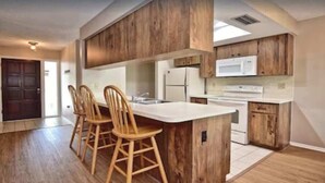 A modern kitchen with wooden cabinets, a central island with bar stools, a microwave, and a refrigerator.