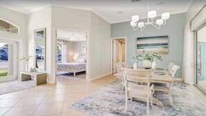 Habitación de hotel moderna con una cama grande, un comedor con mesa y sillas, y vistas al exterior a través de las ventanas.