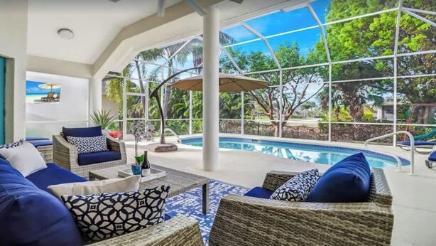 Zona junto a la piscina con mobiliario de mimbre y vistas a la piscina y al follaje.