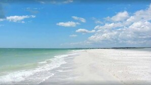 Una playa con agua turquesa cristalina y una amplia orilla de arena bajo un cielo parcialmente nublado.