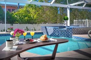 A poolside table with breakfast items, a glass of orange juice, and a flower vase. - 4BR Beach House _ Pool & Jacuzzi _ Beach Access (Marco Island)