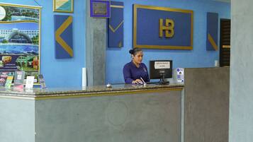 Un mostrador de recepción de hotel con una decoración azul y dorada, un certificado enmarcado en la pared y un cartel que indica los horarios de registro de entrada y salida.