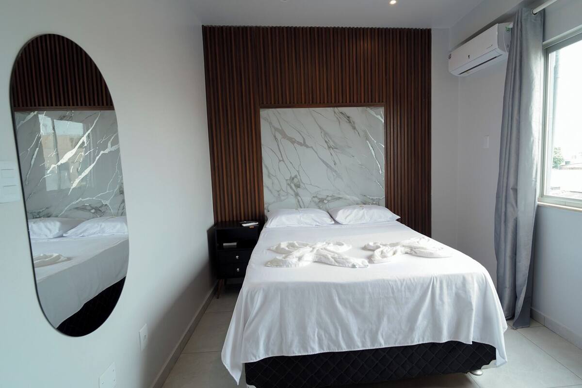 Een moderne slaapkamer met een groot bed, een spiegel, een wand van houten panelen en een airconditioning.