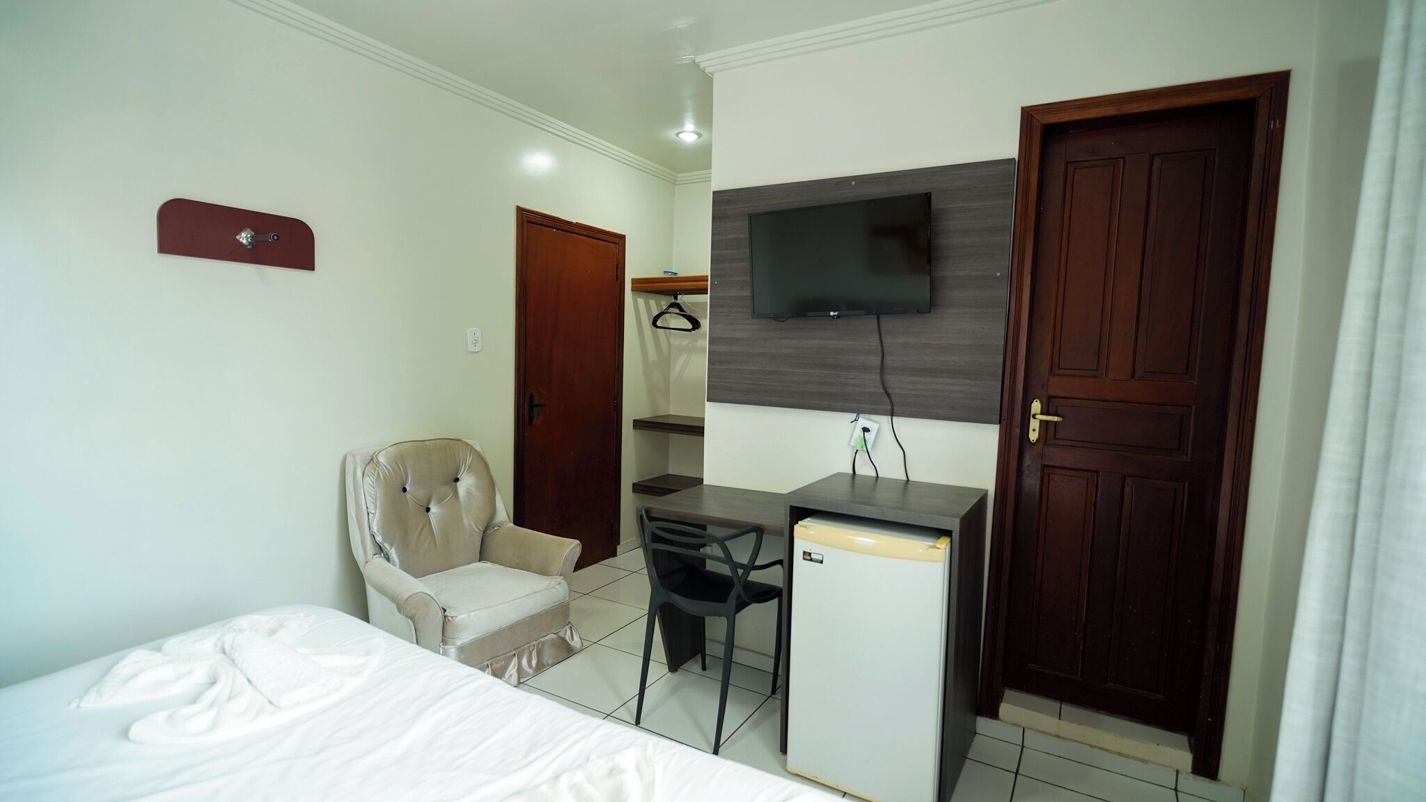 Una habitación de hotel pequeña con cama, escritorio, silla, televisor y armario.