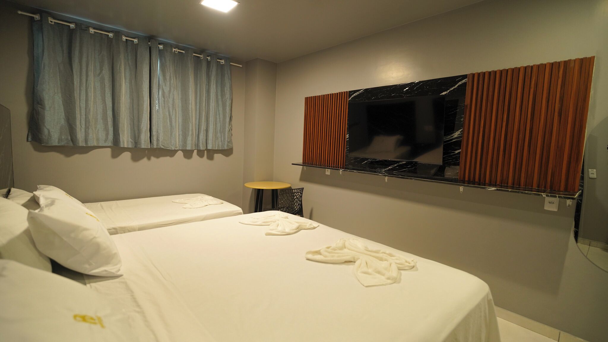 Habitación de hotel con dos camas, una mesita, una silla, un espejo y una ventana con cortinas.