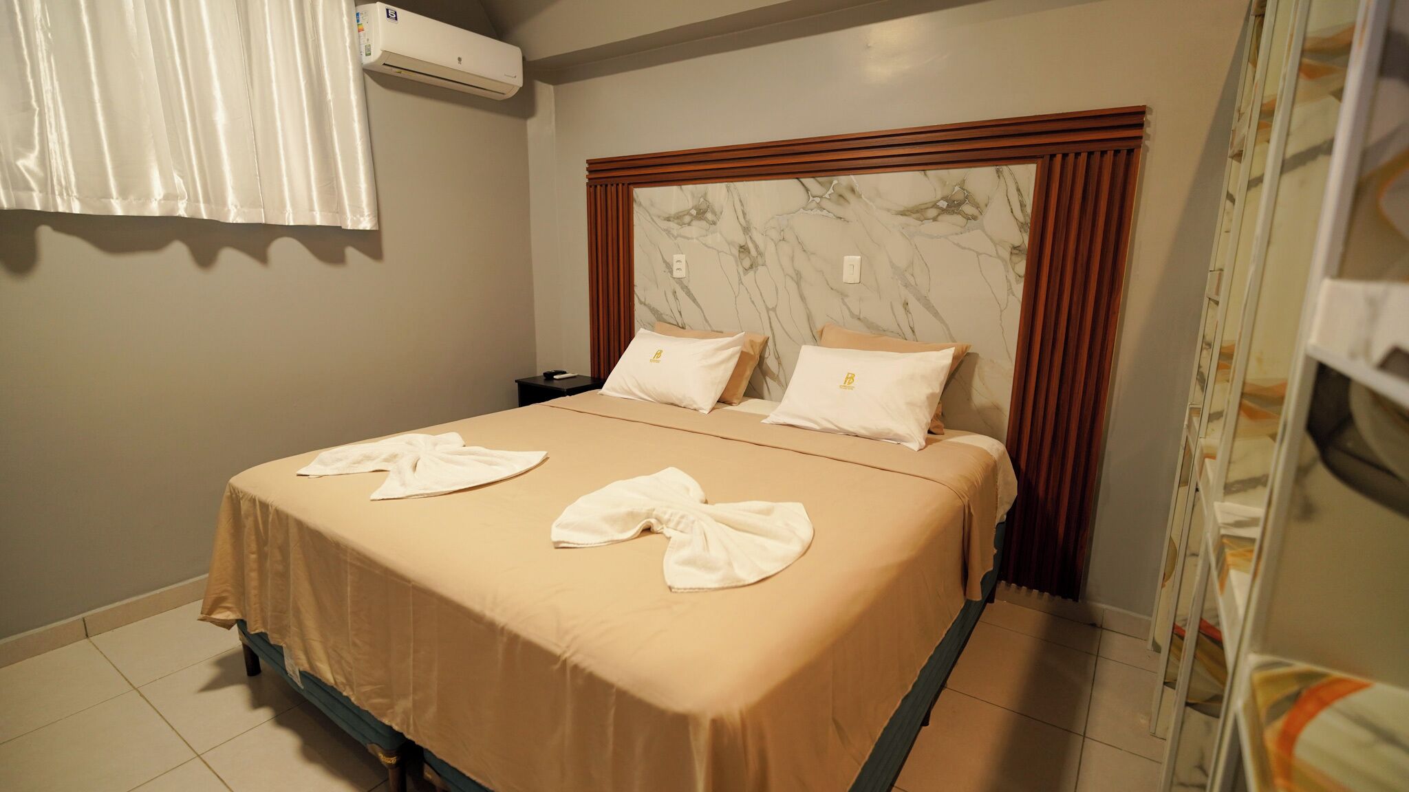 A hotel room with a bed, a nightstand, an air conditioning unit, and a bathroom mirror.