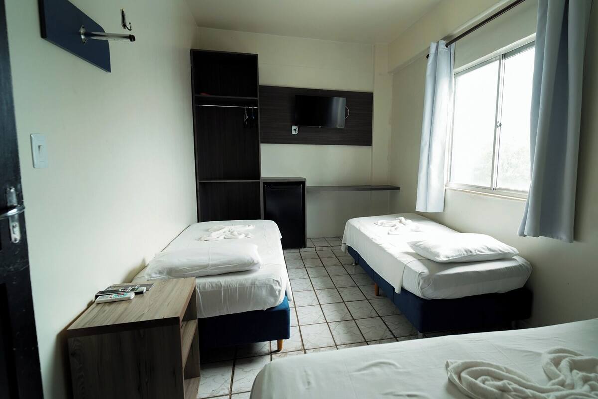 Een kleine, schone kamer met twee bedden, een bureau, een aan de muur bevestigde televisie en een raam met gordijnen.