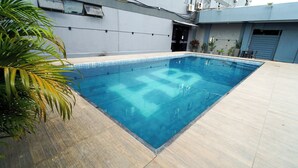 Una piscina rectangular con borde de azulejos, rodeada por una terraza con baldosas de colores claros.