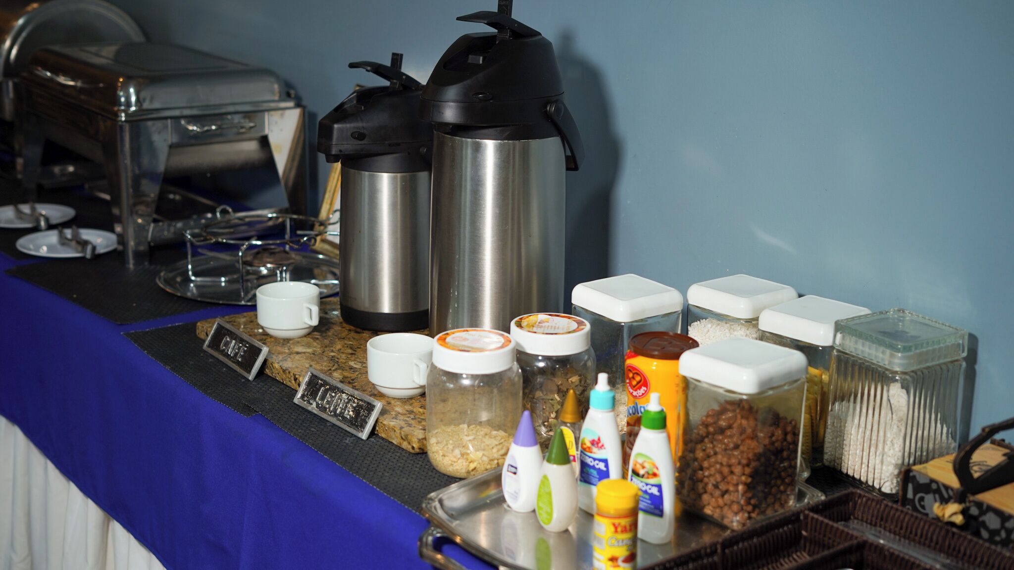 Una mesa de buffet con cafeteras, dispensadores de condimentos y recipientes para alimentos.
