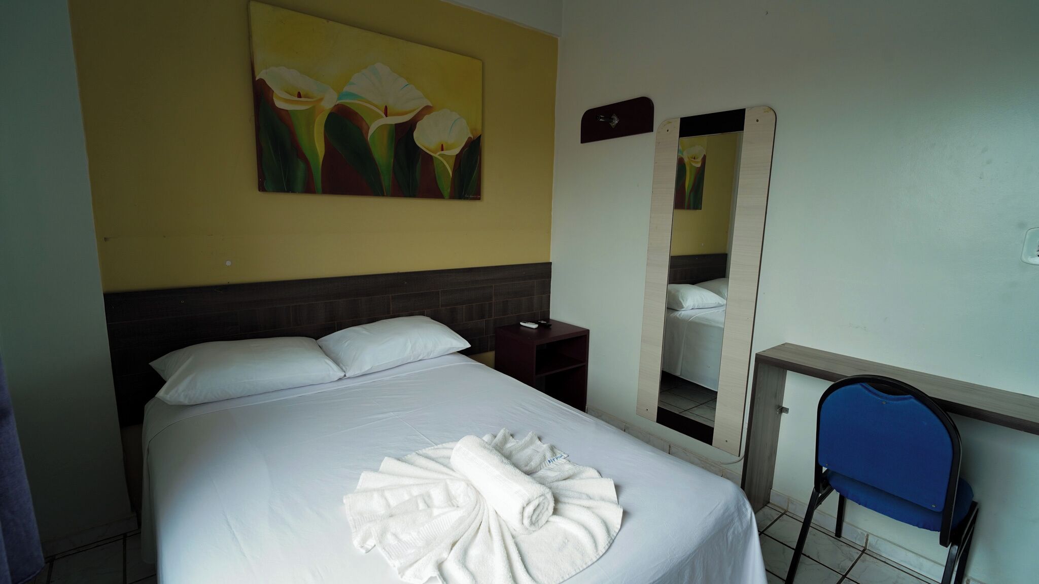 A hotel room with a bed, a nightstand, a mirror, and a chair.