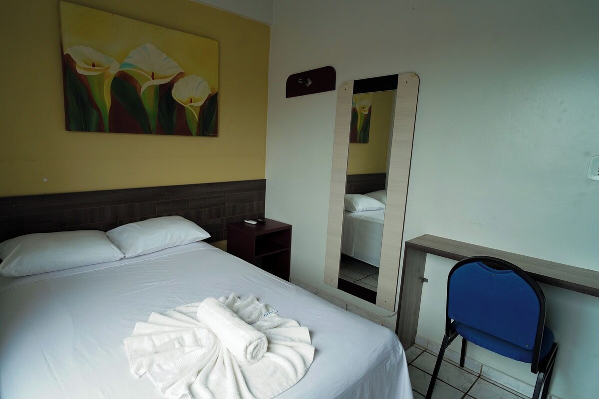 A hotel room with a bed, a nightstand, a mirror, and a chair.