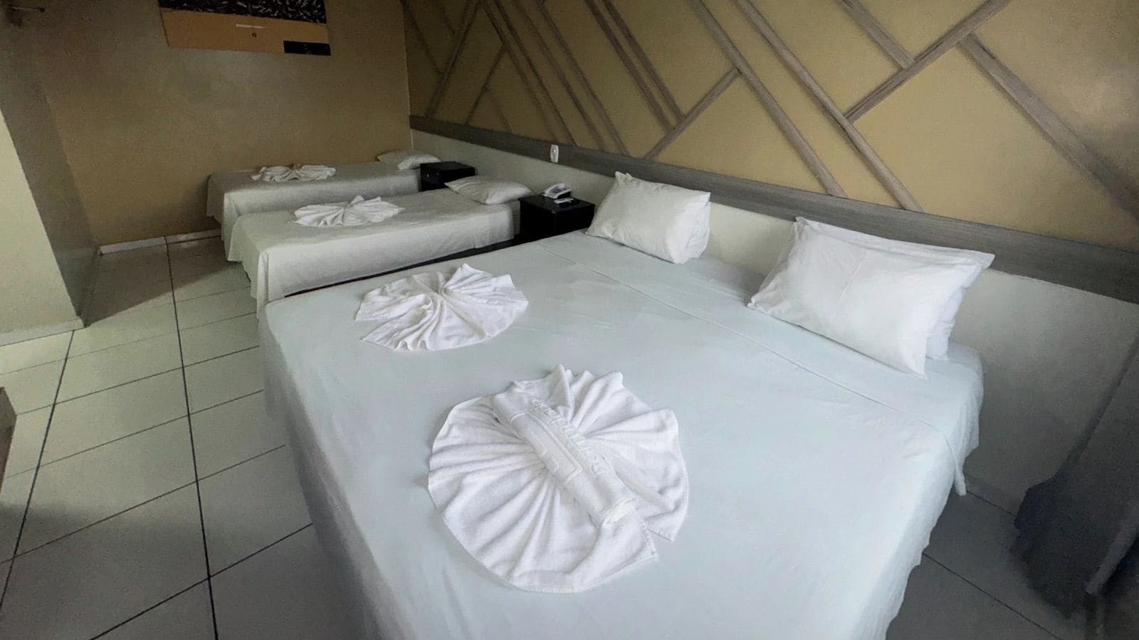 A hotel room with a large bed, two smaller beds, and a headboard with a geometric design.