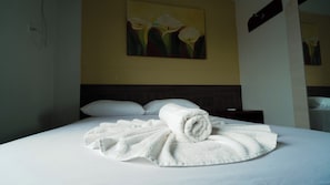 Quarto de hotel com cama bem arrumada, pintura de flores na parede e mesa de cabeceira com abajur.