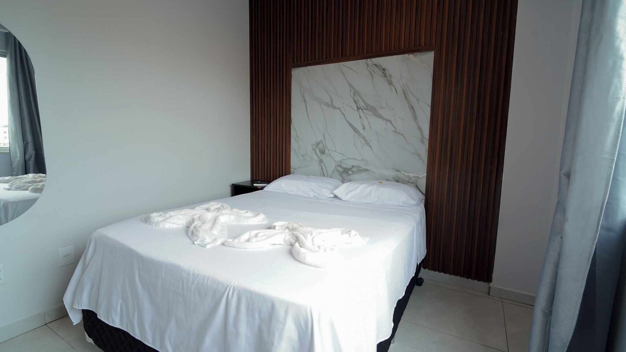 A modern bedroom with a large bed, a marble headboard, and a view of the city.