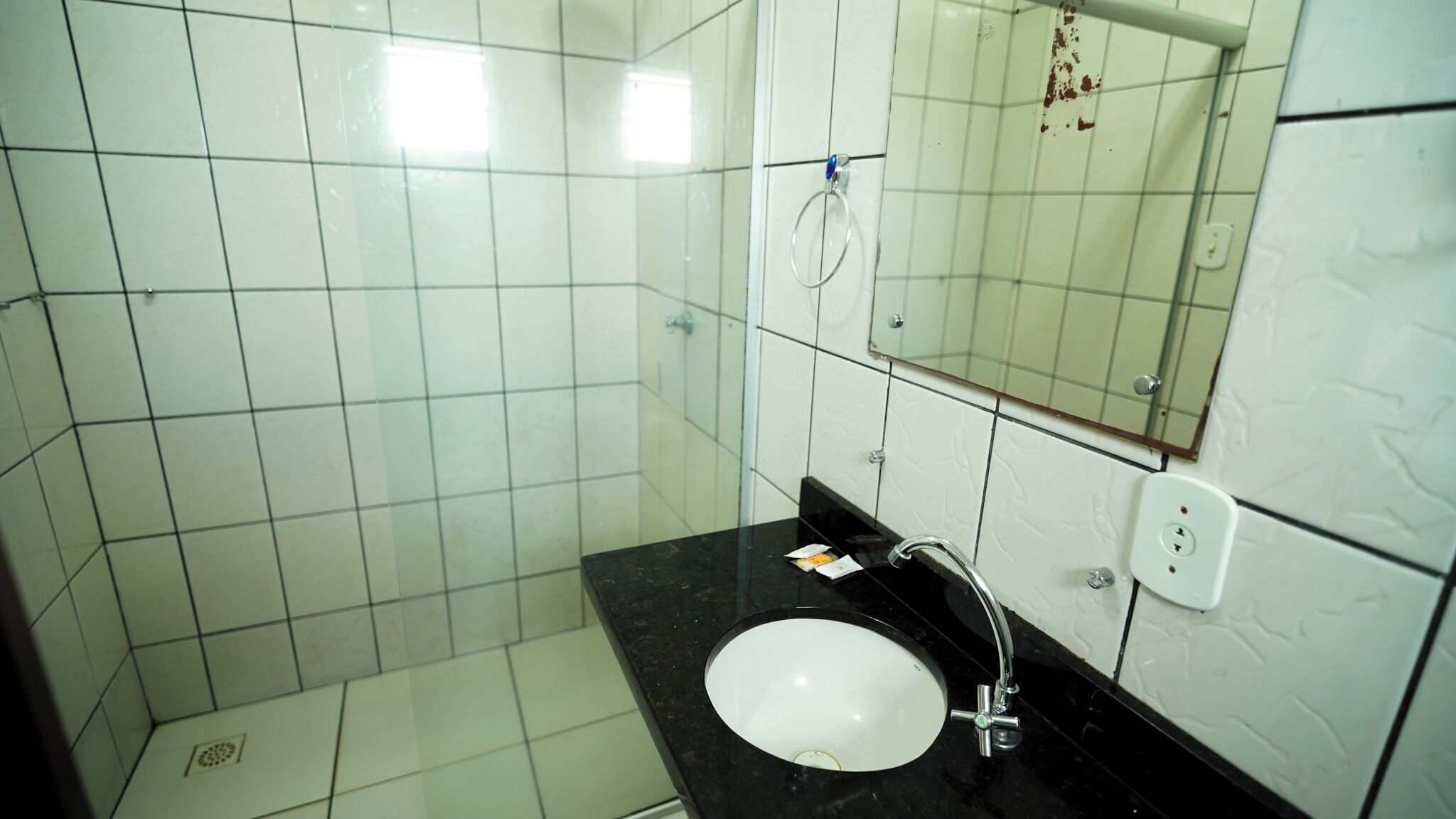 Een badkamer met witte betegelde wanden, een zwart aanrecht, een wit wastafel, een spiegel en een douchehoek.