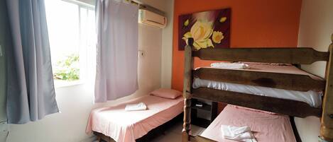 A dormitory room with bunk beds, a window with curtains, an air conditioning unit, and a painting on the wall.