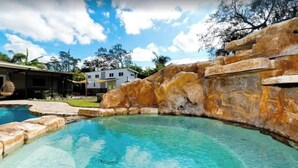 A swimming pool with clear water, surrounded by stone structures and a white building in the background.