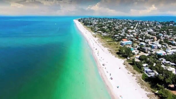 An aerial view of a coastal area with a long stretch of beach and a densely populated residential area.