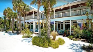 A two-story building with a balcony on the upper floor, surrounded by palm trees and greenery.