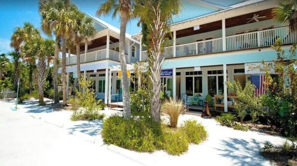 A two-story building with a balcony on the upper floor, surrounded by palm trees and greenery.