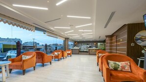 A hotel lobby with orange chairs, a reception desk, and a view of the city through large windows. - Royal Boutique Hotel (Khamis Mushait)