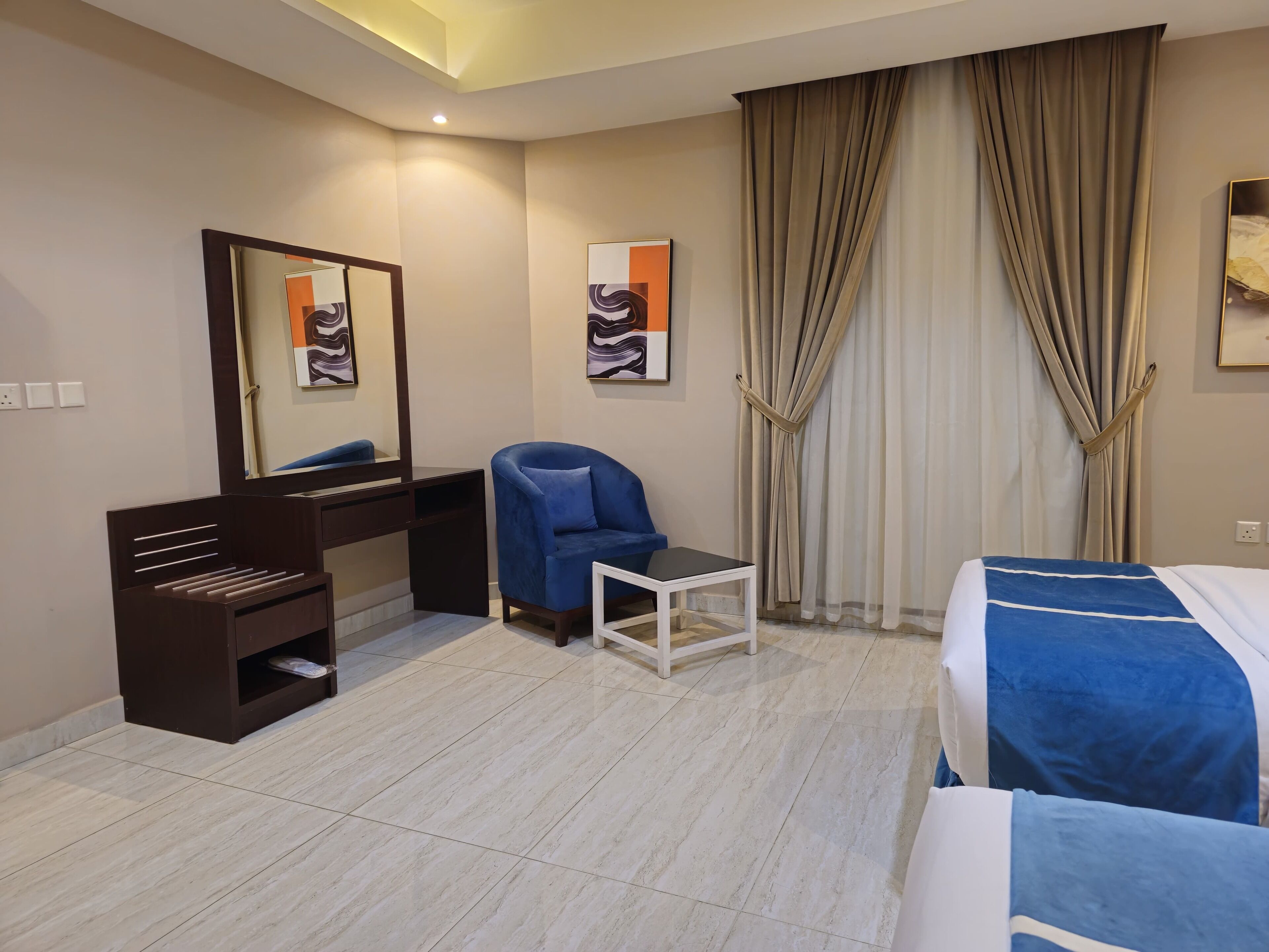 A hotel room with a bed, a desk with a chair, a mirror, and two paintings on the wall.