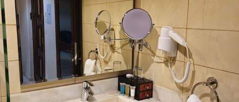 Un baño con lavamanos de mármol, dos espejos, un secador de pelo y un perchero para toallas.