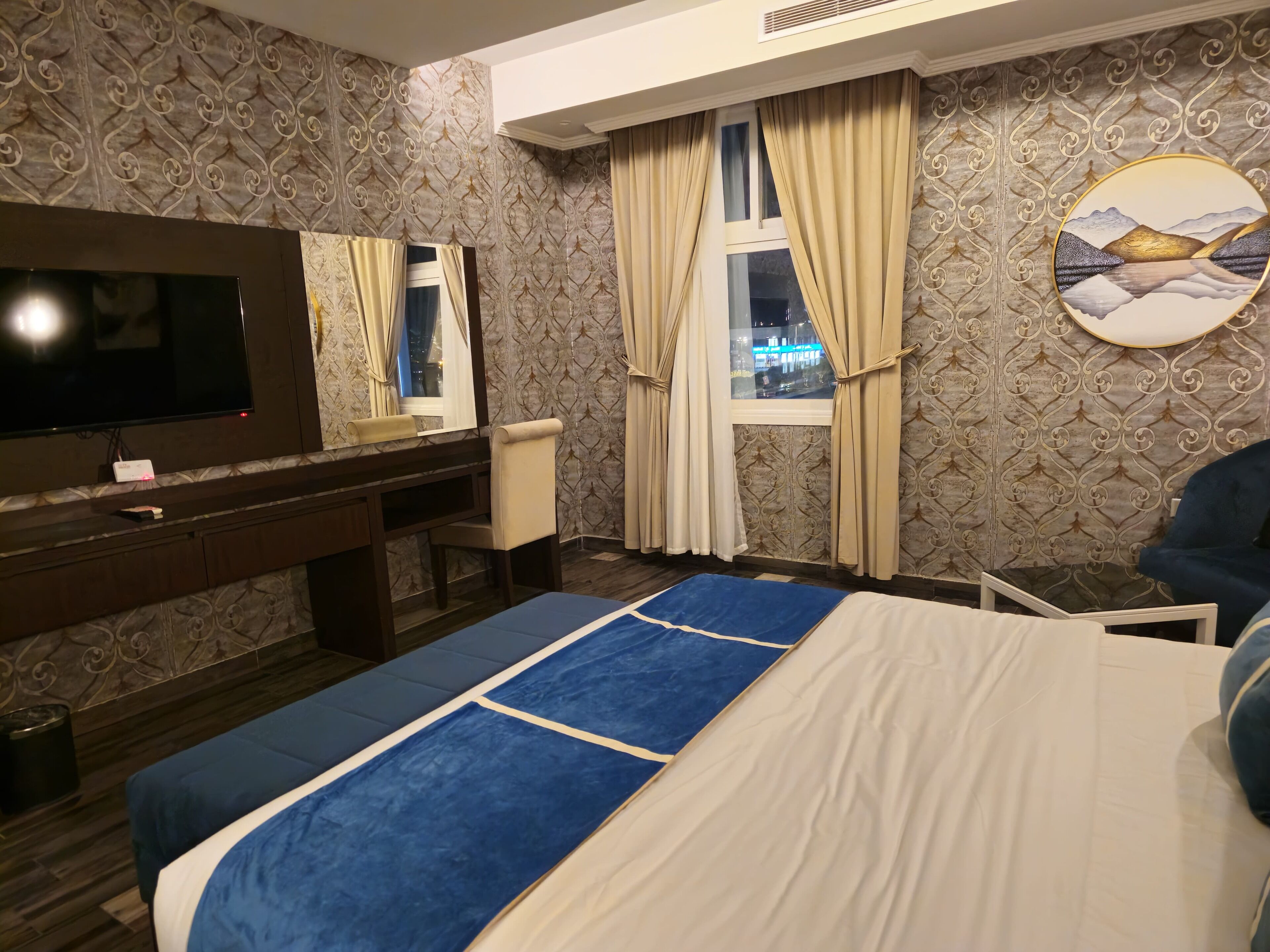A hotel room with a bed, a desk, a chair, a TV, and a window with curtains.