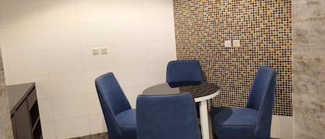 Una sala de reuniones pequeña con una mesa redonda, cuatro sillas azules, una pared de mosaicos de azulejos y suelo de madera.